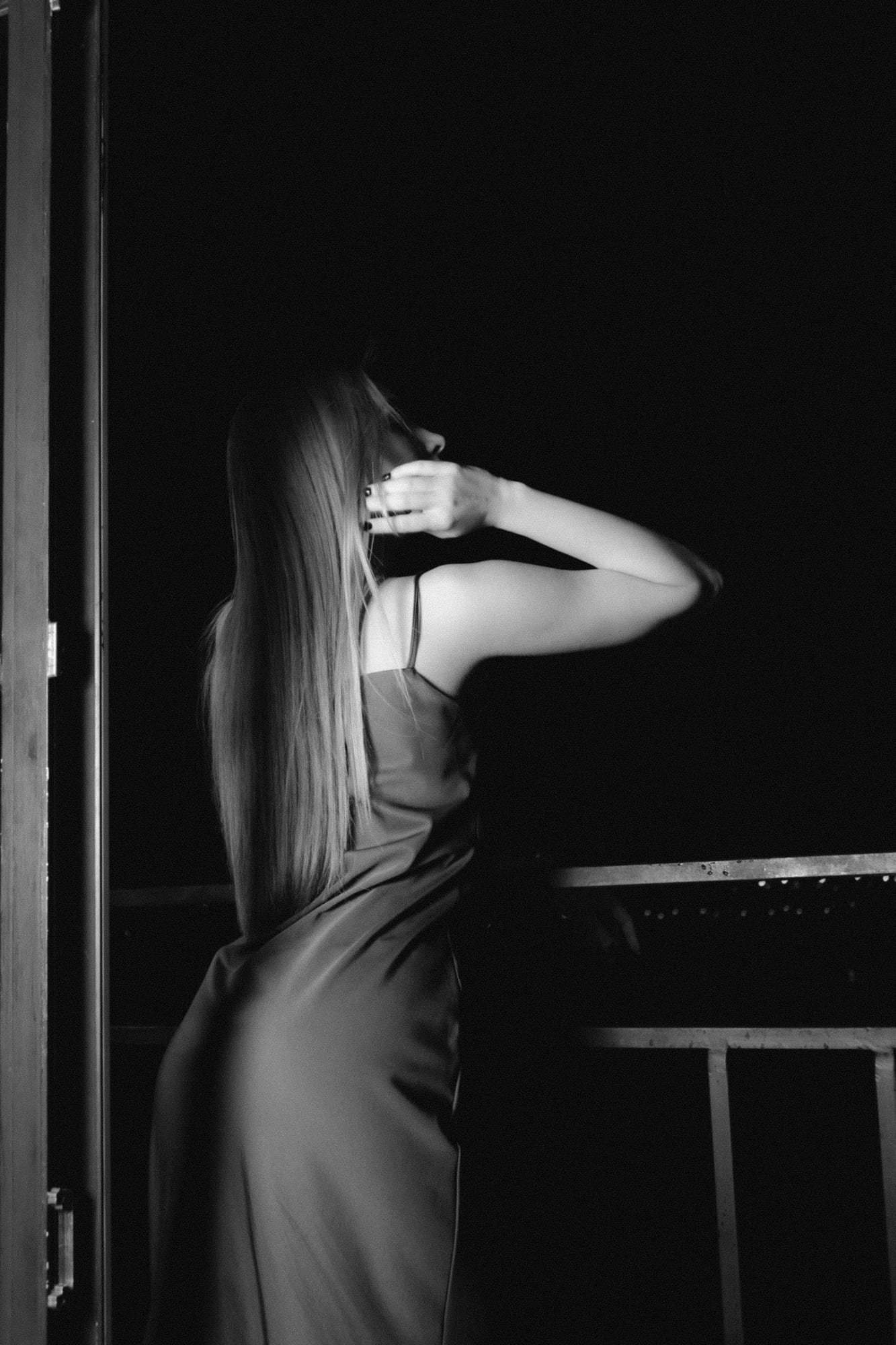 Woman seen from behind in a satin slip on a balcony at night